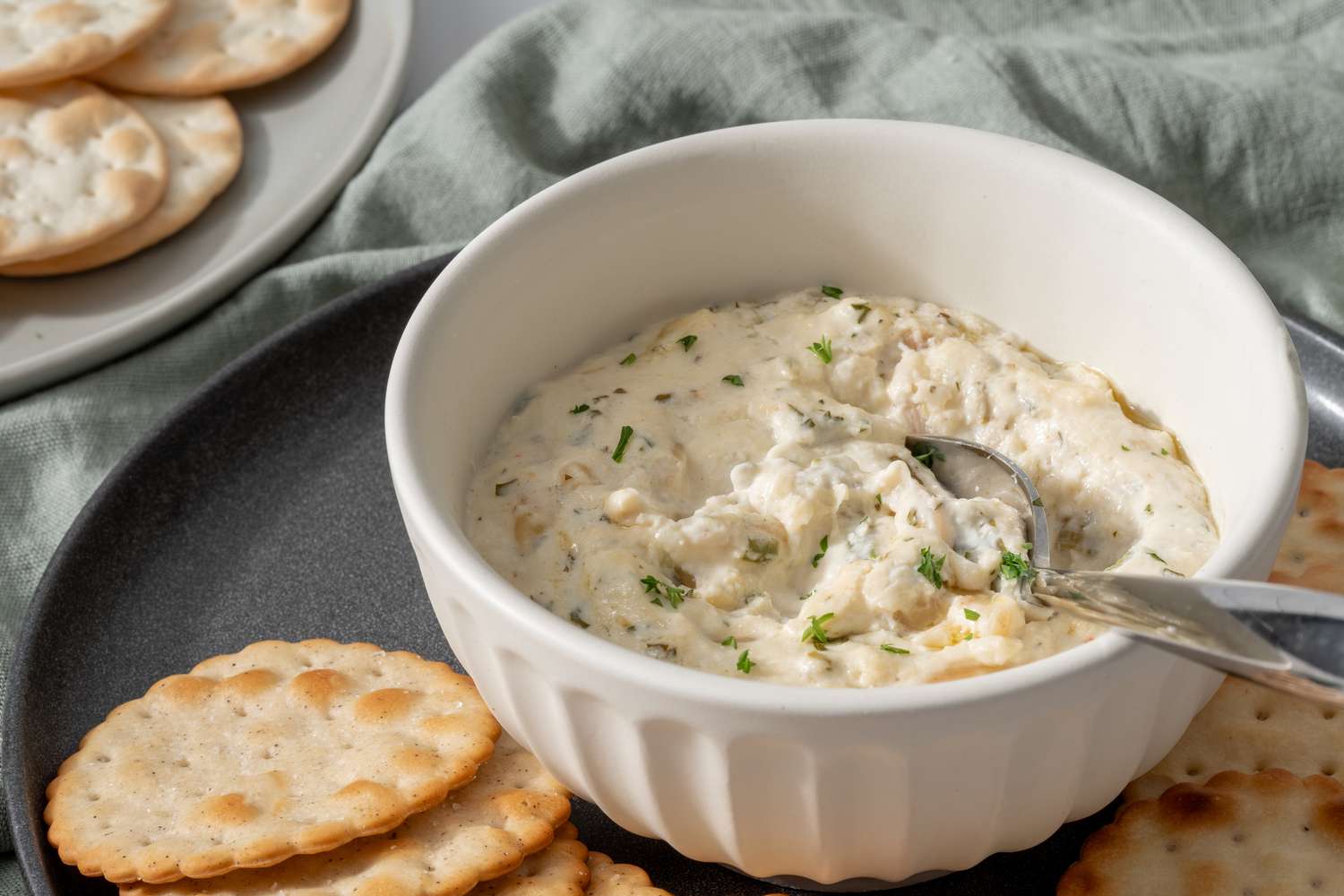 Side view of a bowl of hot crab dip with a spoon and round crackers.