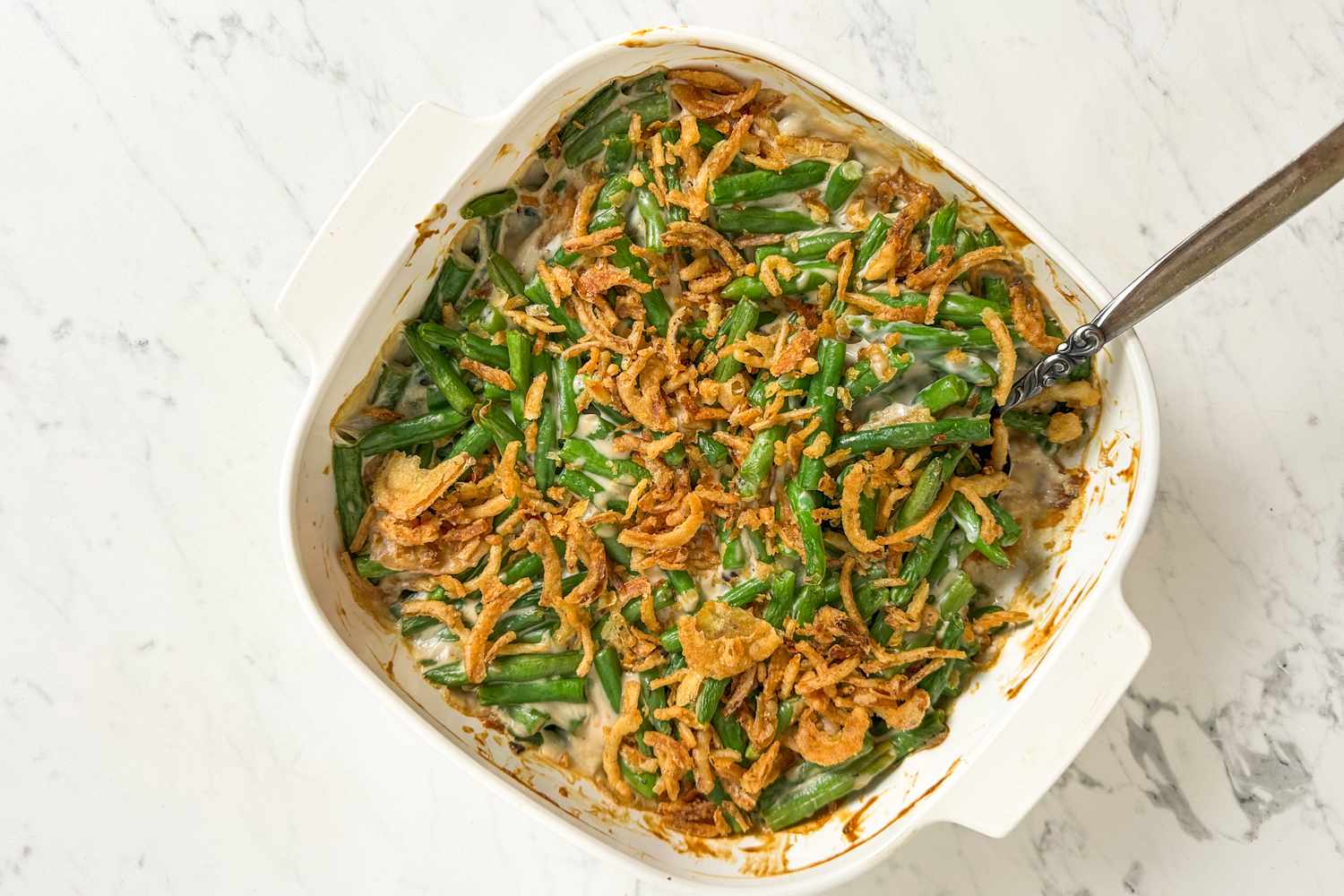 Green bean casserole in a white dish with a spoon
