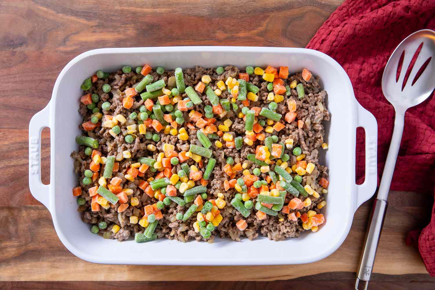ground beef topped with frozen veggies in a baking dish for Classic Tater Tot Hotdish