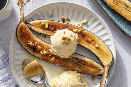 Caramelized bananas served with scoops of ice cream topped with chopped nuts on a white plate