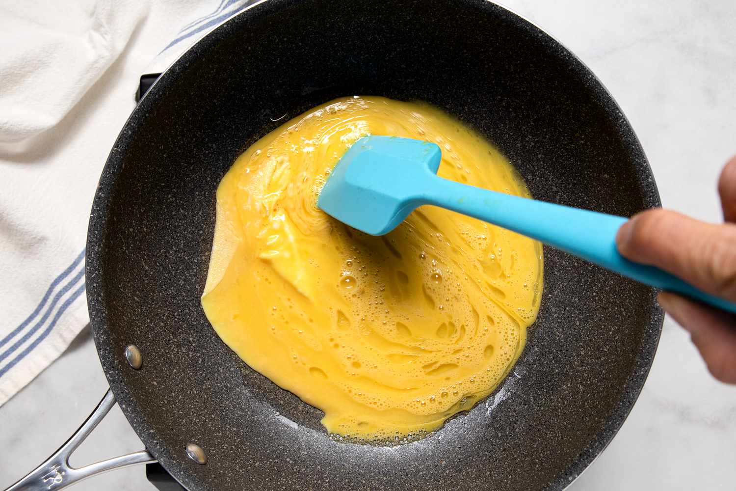 Overhead of a hand holding a spatula scrambling eggs in a pan