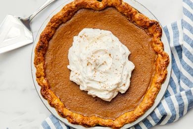 Pumpkin pie topped with whipped cream displayed on a table with a pie server and a striped cloth napkin