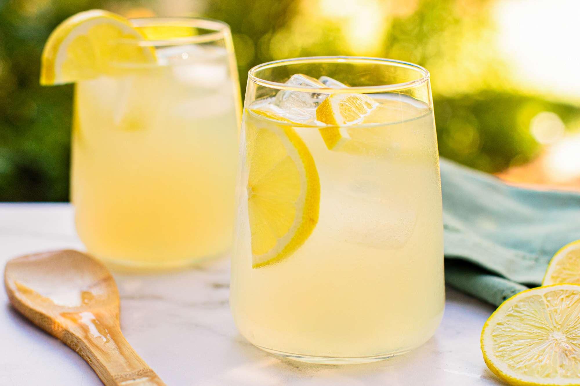 Two glasses of lemonade on a table with slices of lemons and a wooden spoon