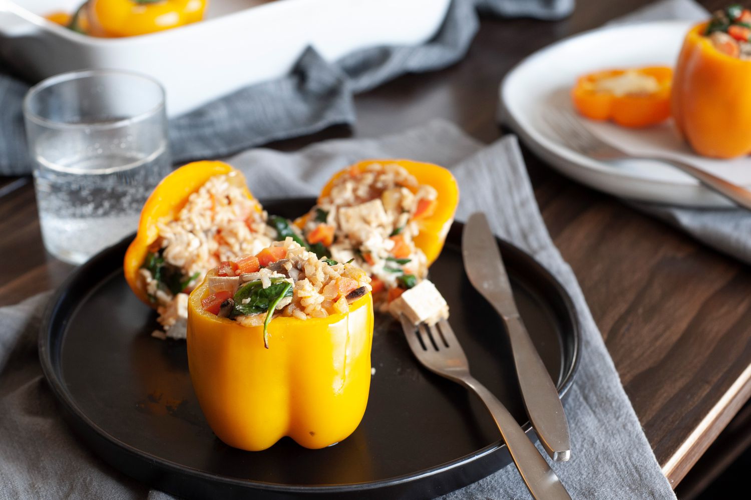 Cheesy rice, tofu, and mushroom stuffed peppers on a black plate