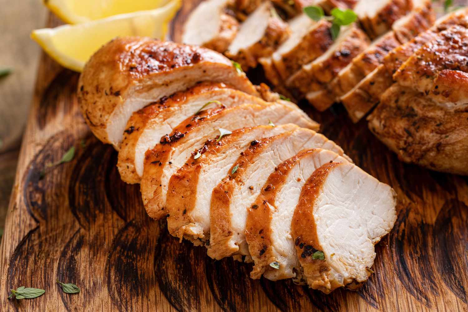 grilled chicken (sliced) on a cutting board with lemon wedges