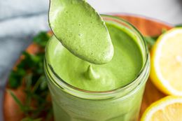Green Goddess Dressing Dripping from a Spoon into a Jar with More Dressing