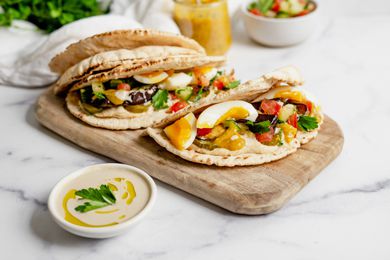 Sabich Sandwiches on a Wooden Plank Next to a Bowl of Tahini