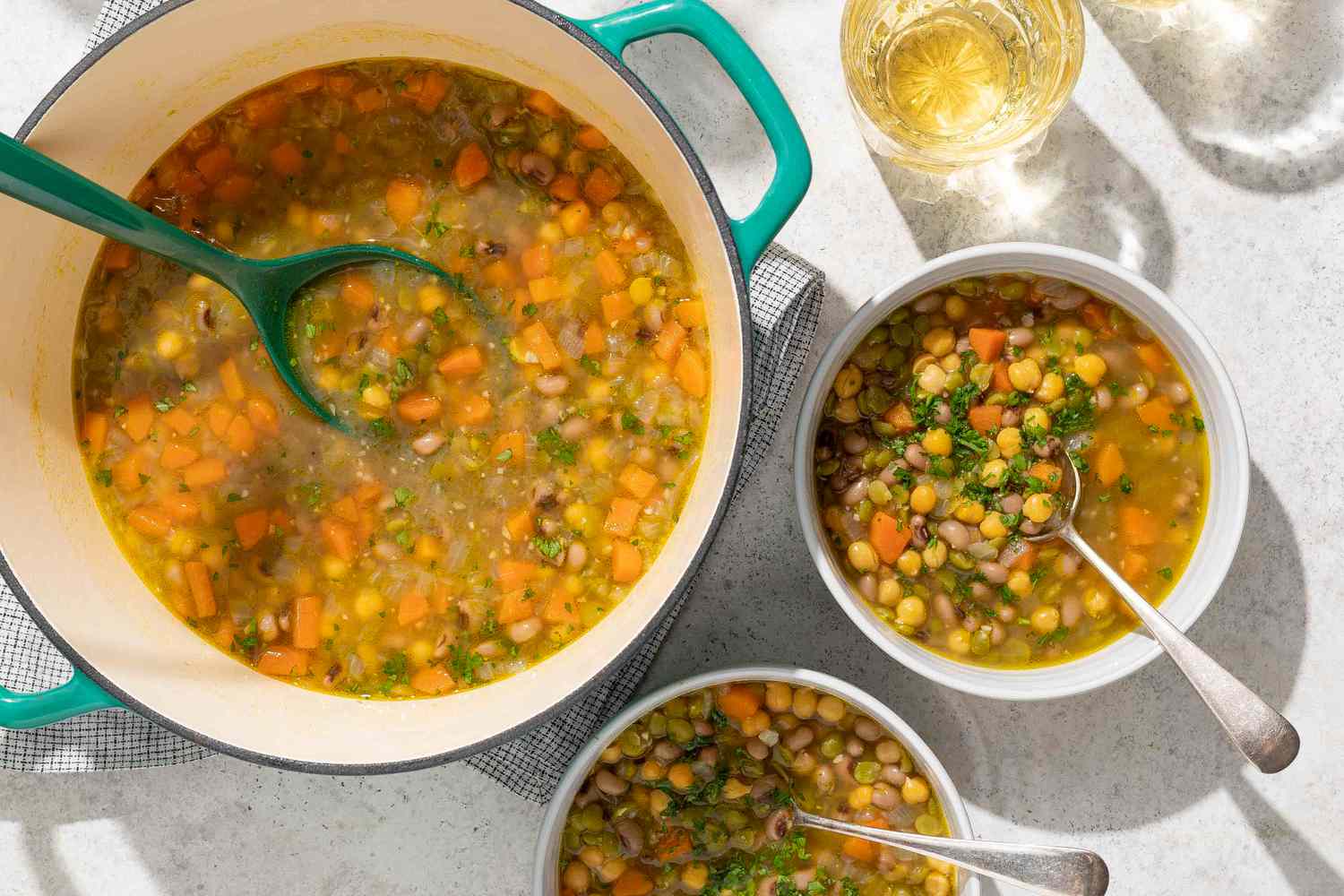A pot and two bowls of threepea soup with serving spoons visible on a table