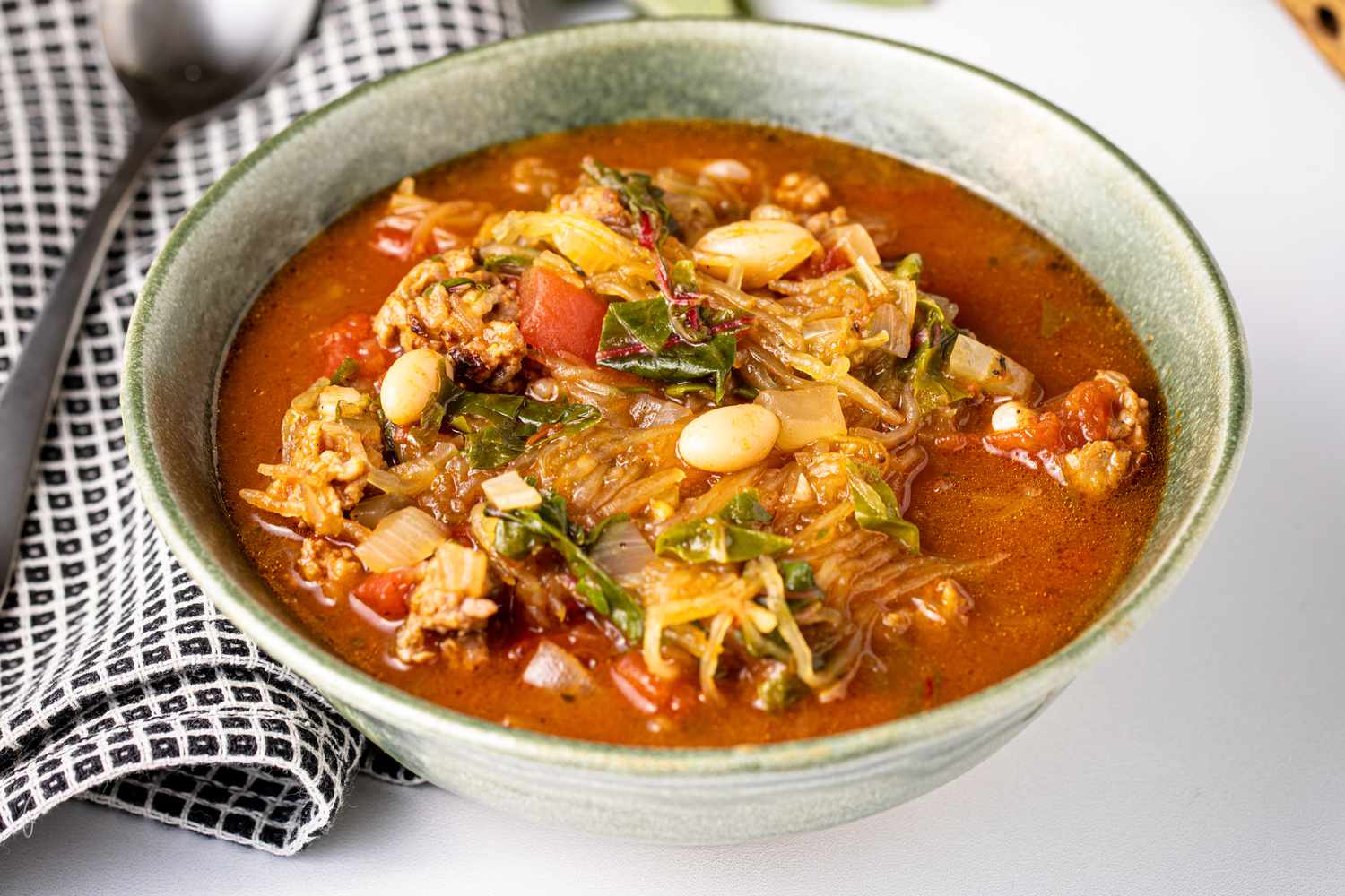 Spaghetti Squash Soup with Italian Sausage in a Bowl Next to a Kitchen Towel and a Spoon
