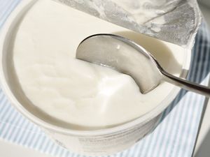 A spoon dipped into a container of yogurt on a striped surface