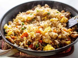 A black skillet with prepared pork fried rice recipe inside. Steam is coming up from the dish and a spatula is resting in the rice on the left side.