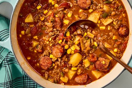 Overhead view of a dutch oven of cowboy stew with a ladle and a cloth napkin all on a marble countertop