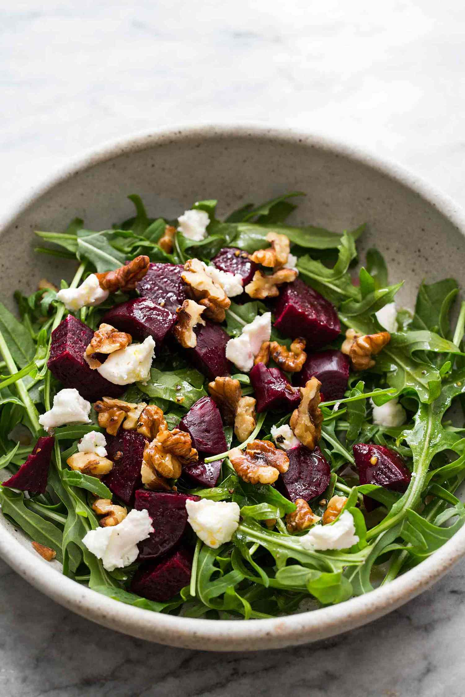 Arugula salad topped with roasted beets goat cheese and walnuts in a bowl