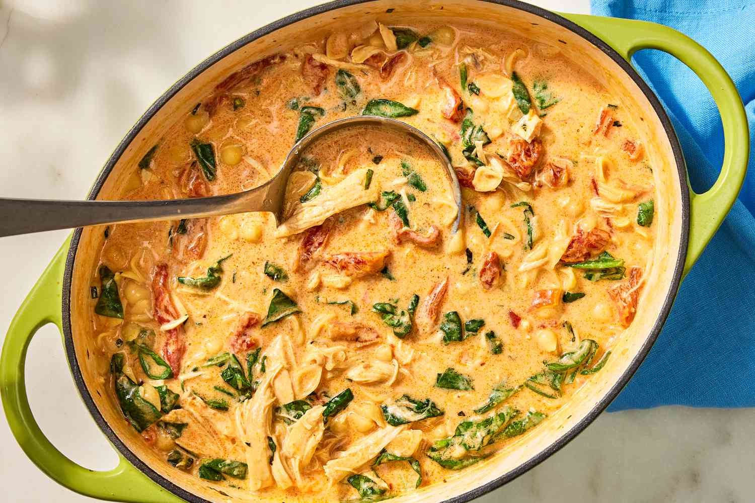 Overhead view of a large green dutch oven of Marry Me Chicken Soup with a ladle