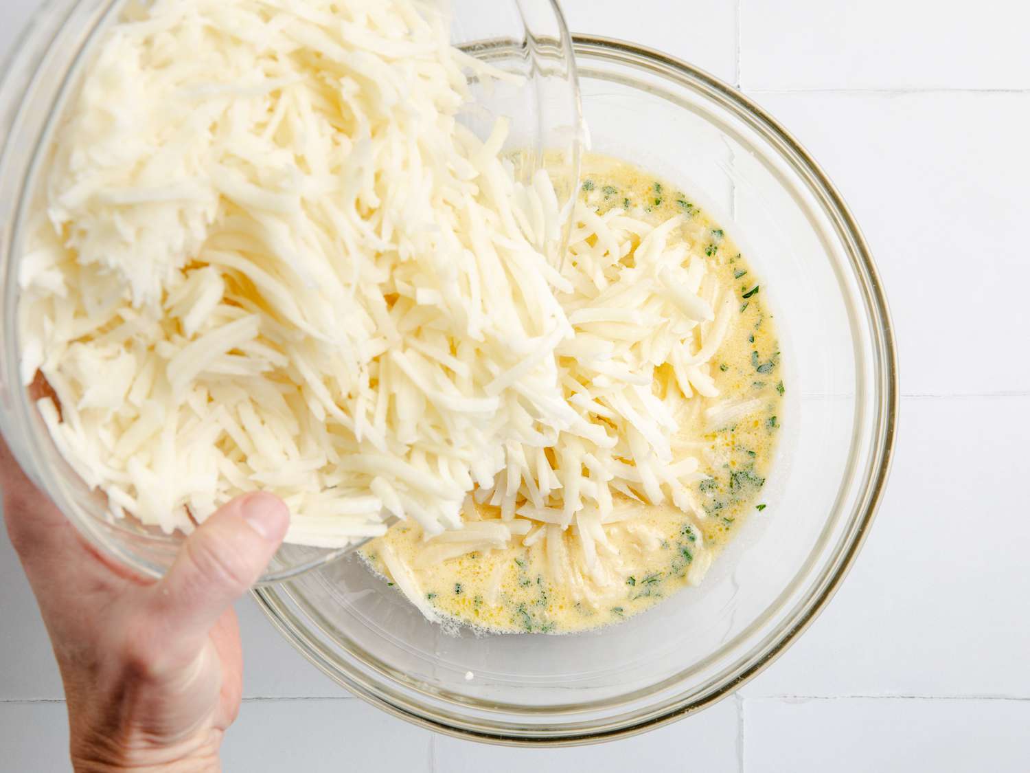 hand pouring shredded potatoes into sauce