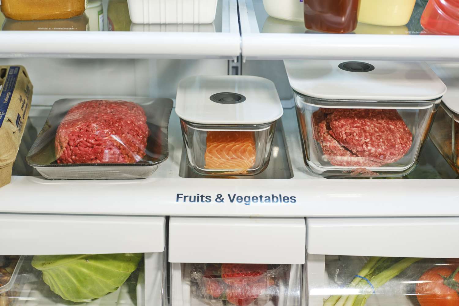 A refrigerator shelf with ground meat, salmon, and vegetables in storage containers