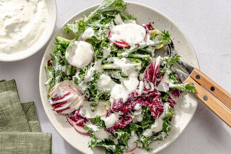 Plate with salad topped with creamy dressing fork and knife on the side napkin nearby