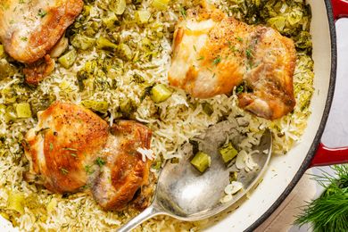 Cooked chicken thighs on a bed of rice with chopped pickles and herbs in a skillet