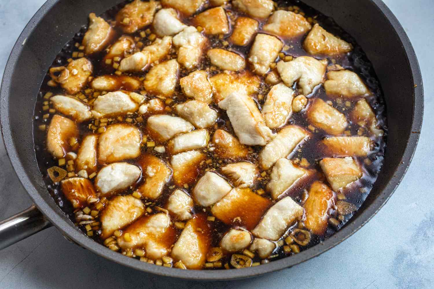 Chicken and sauce simmering in a skillet to make Sweet and Tangy Bourbon Chicken.