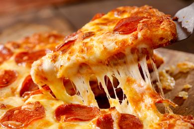 A slice of pepperoni pizza being lifted with melted cheese stretching