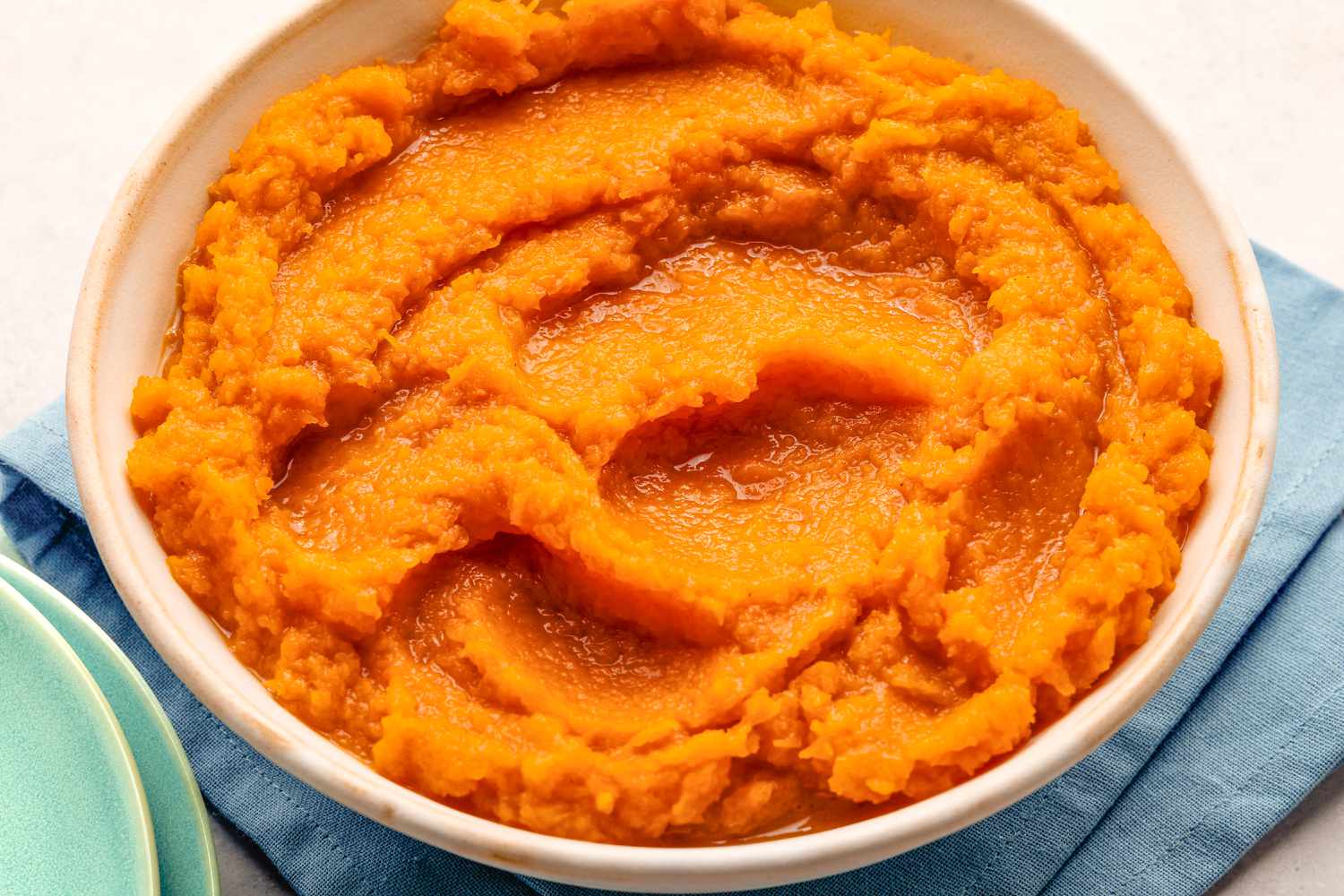 Overhead view of a white bowl of butternut squash resting on a blue table napkin