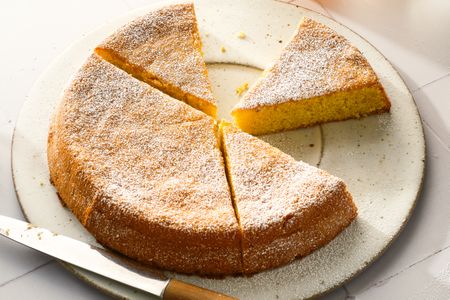 A sliced flourless lemon almond cake on a plate with a knife