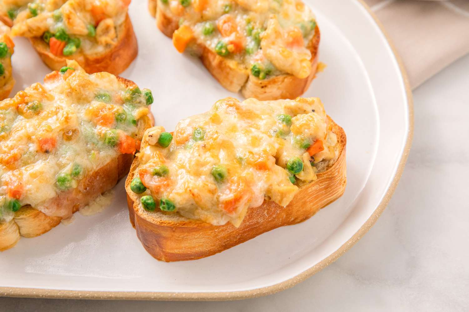 Chicken pot pie toasts with peas carrots and melted cheese on bread slices served on a plate