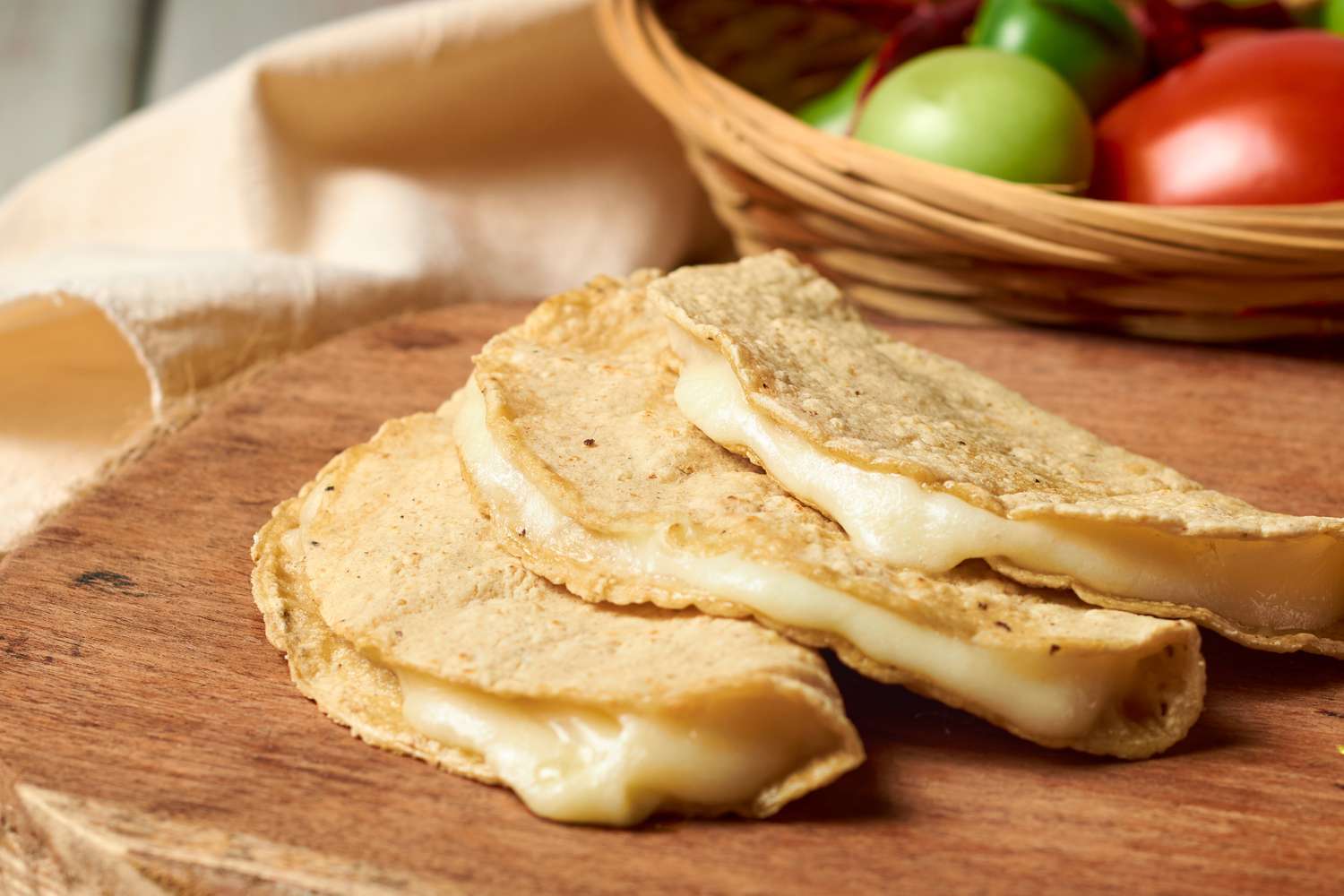 Cheese quesadillas on a wooden surface with a basket of fresh vegetables nearby