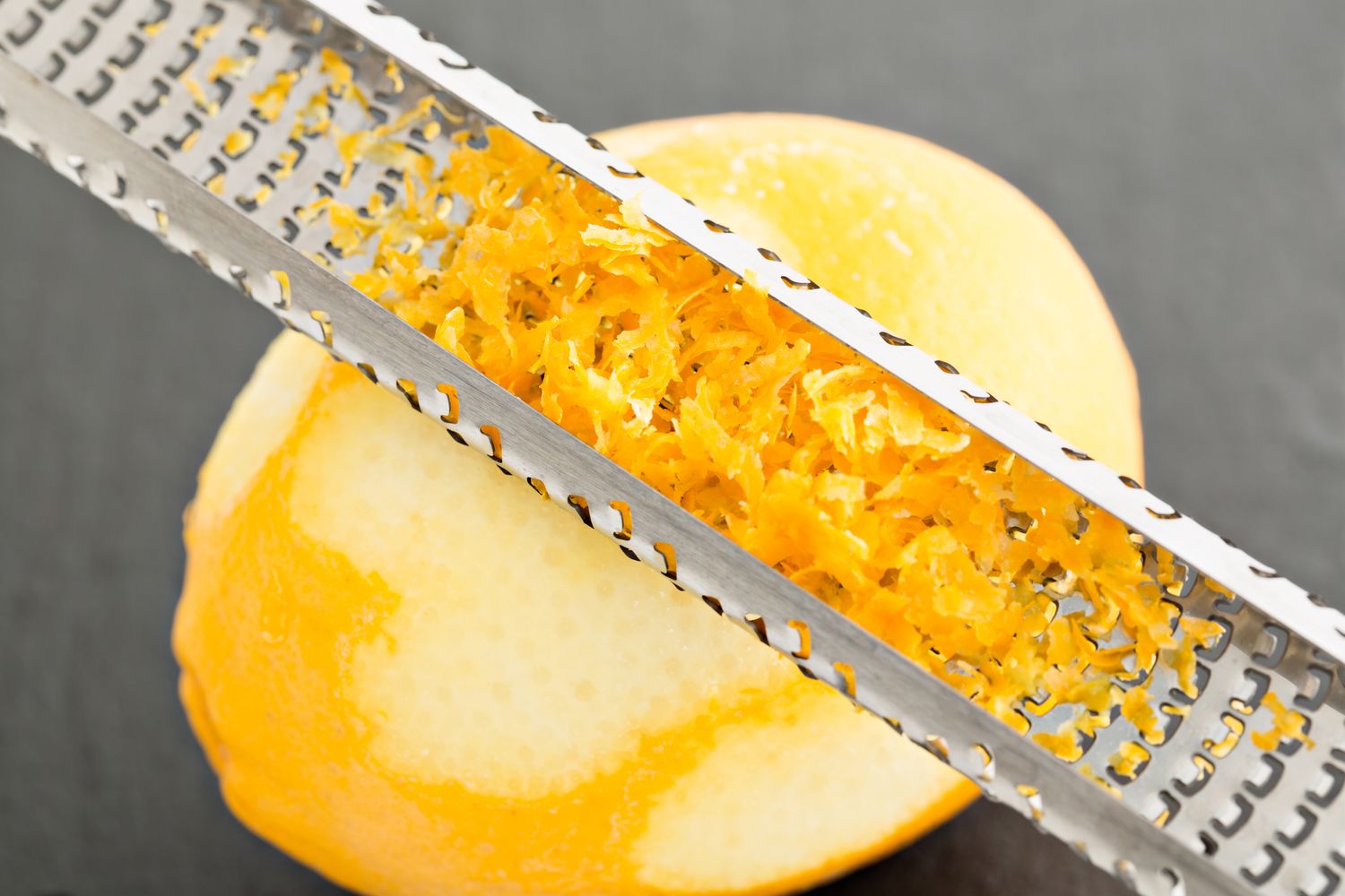 A citrus zester grating the peel of a lemon for zest collection