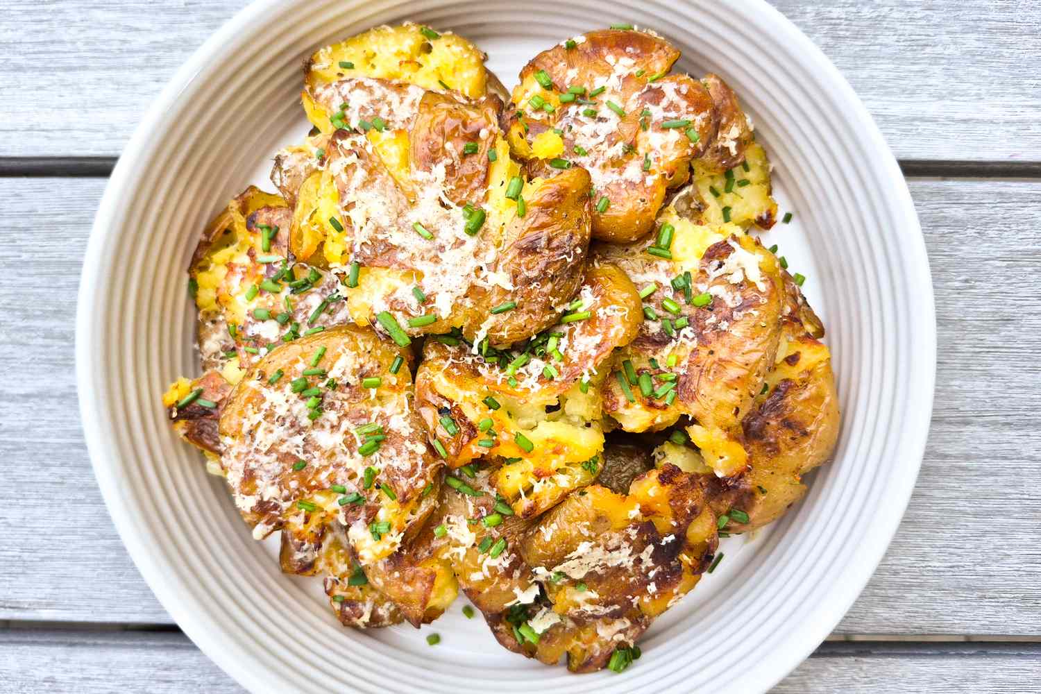 A plate of smashed potatoes garnished with herbs and cheese