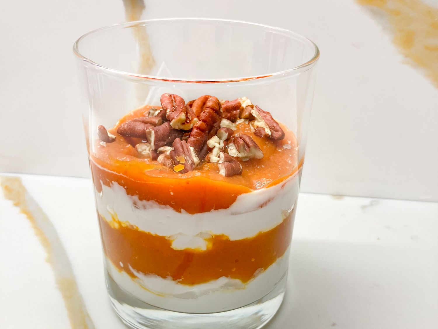 Layered yogurt and pumpkin dessert topped with pecans in a glass