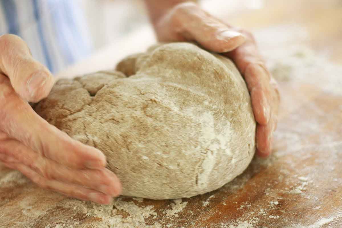 Hands to the side, shaping rye bread dough on a flour-dusted wooden table