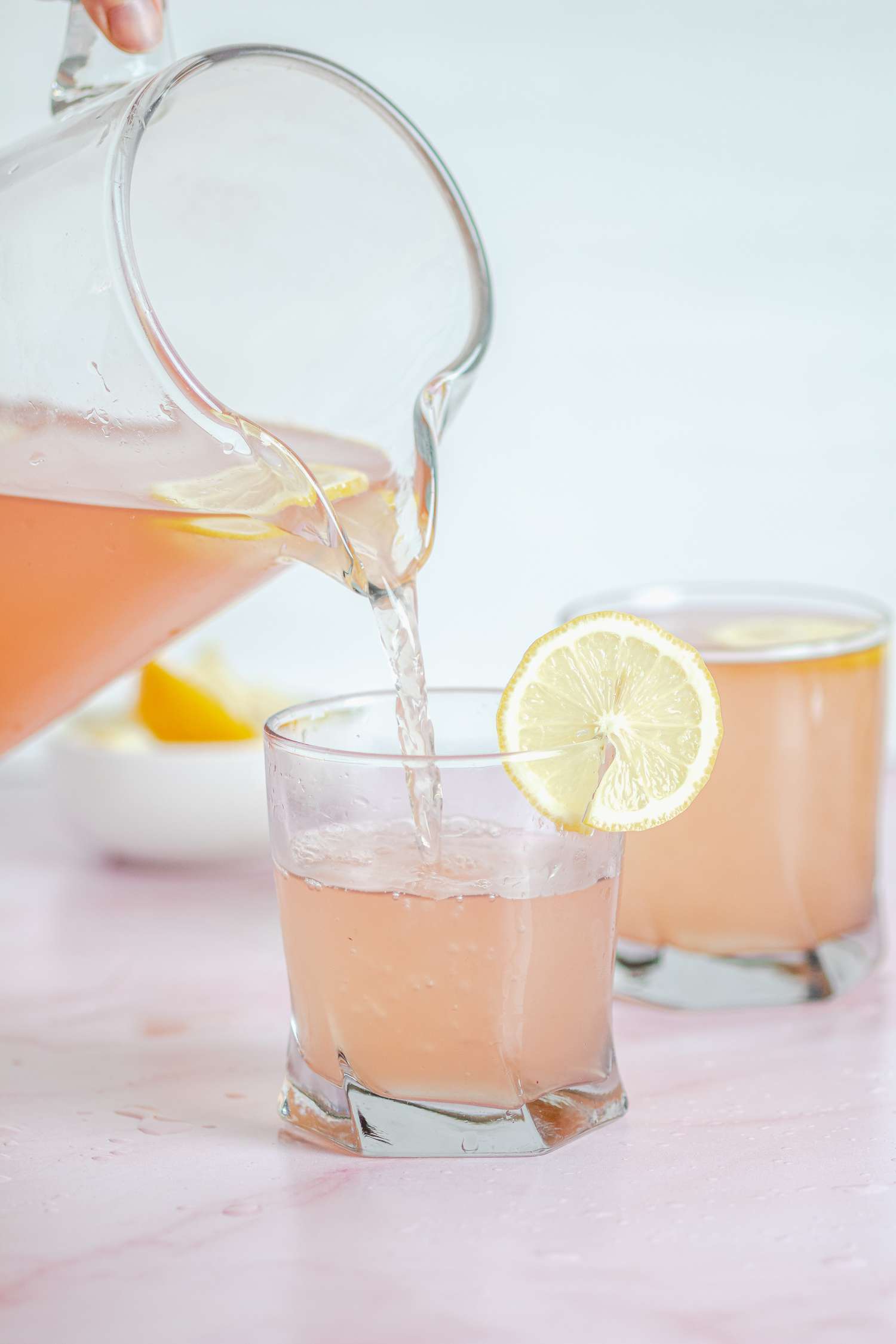 Pouring a glass of pink lemonade from a pitcher.