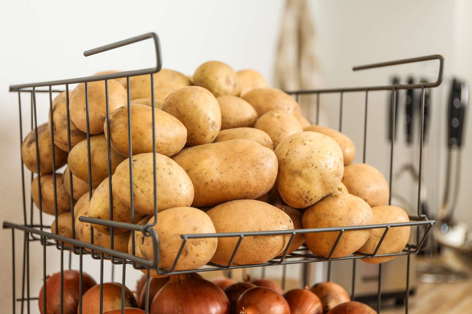 Pile of whole potatoes in a metal wire basket with a kitchen blurred in the background