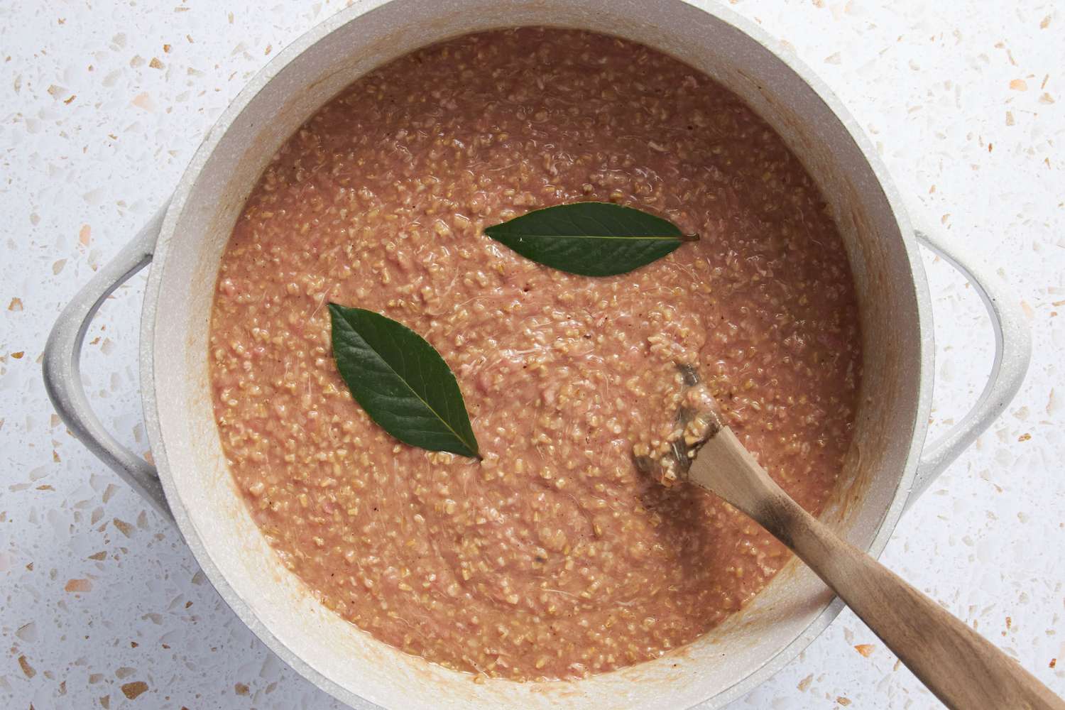 Meat Mixture and Bay Leaves Mixed Into Pot of Oats With a Spoon 