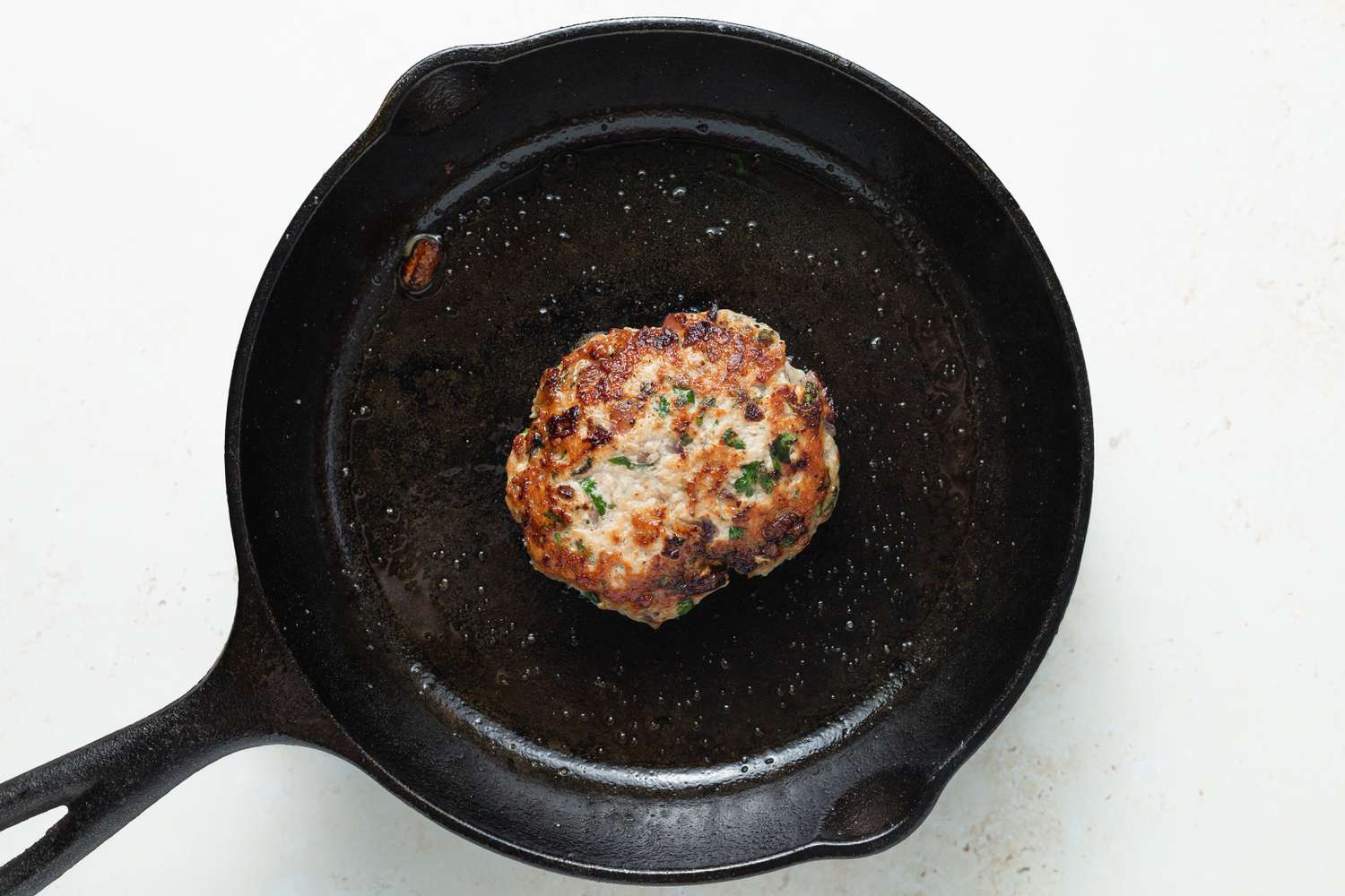 A cast iron skillet pan frying a turkey burger for a best turkey burger recipe.