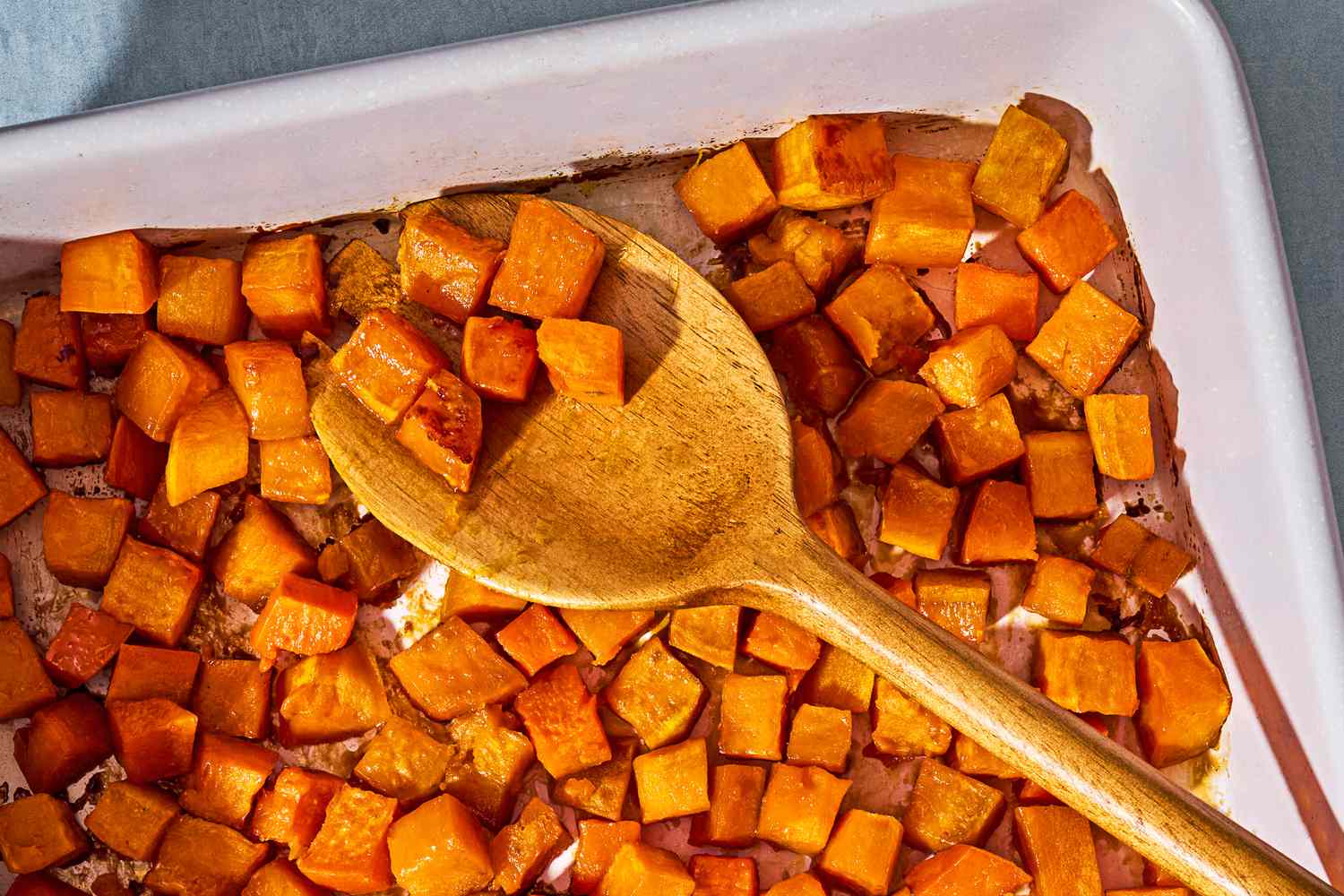Overhead view of a baking dish of cubed baked sweet potatoes and wooden serving spoon