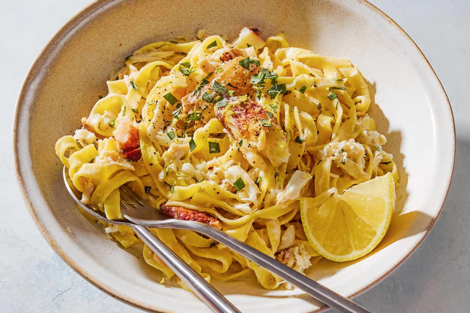 A bowl with a creamy crab fettuccine pasta, with a lemon wedge and chopped fresh tarragon as garnish