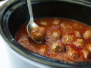 Meatballs in a slow cooker filled with tomato sauce with a spoon lifting a meatball out of the sauce.