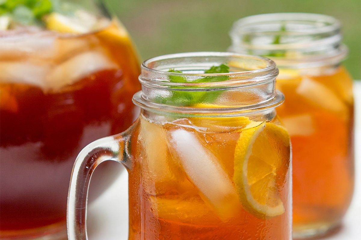 Two mason jars and a pitcher of iced tea, garnished with lemon slices and mint