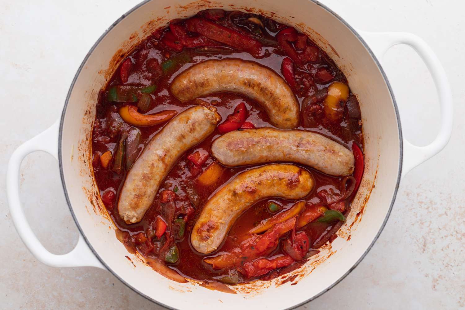 Overhead view of a dutch oven with polish sausage, peppers, and onions cooking
