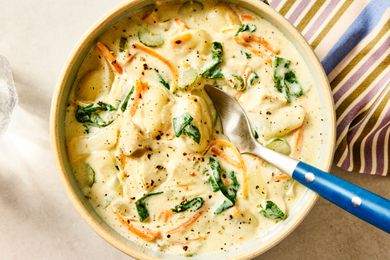 A bowl of creamy gnocchi soup with vegetables garnished with spinach and served with a spoon