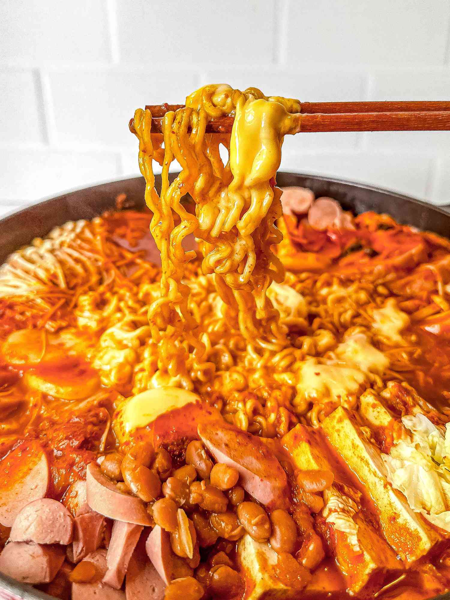 Chopsticks lifting some ramen from the pot of budae jjigae (army base stew)