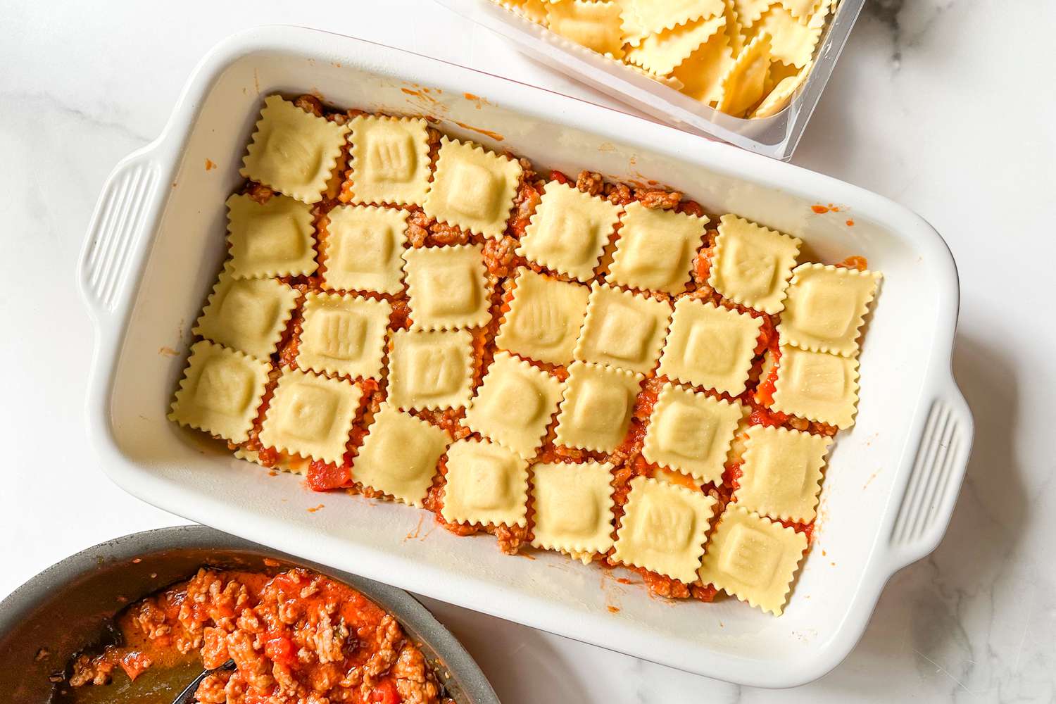 layer of ravioli added to to a casserole dish after a layer of tomato sauce with meat pieces 