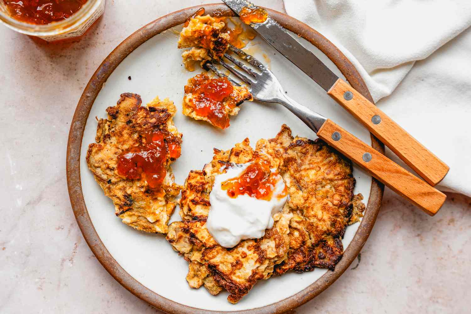 Overhead view of a plate of Matzo Brei Pancakes with a fork and knife on a pink marble countertop