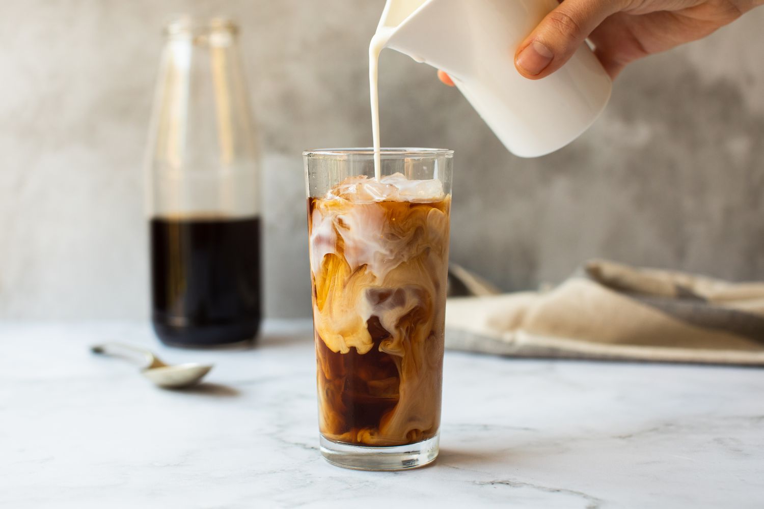A creamer being Poured into a Glass of Cold Brew Coffee
