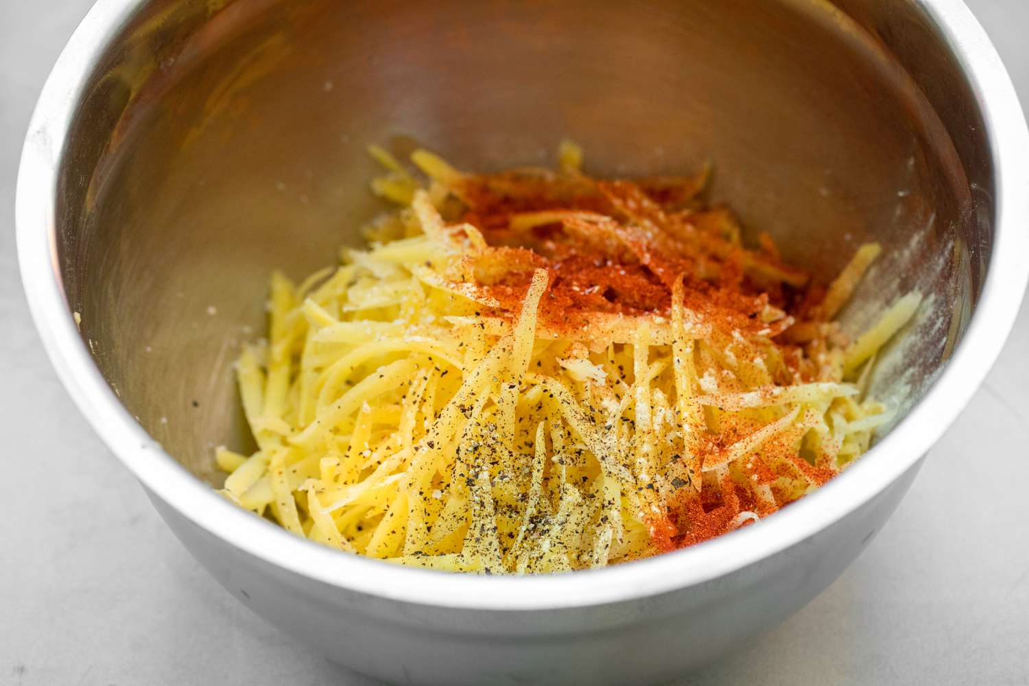 Hash Brown Potatoes in Bowl with Paprika, Salt, and Pepper for Air Fryer Recipes