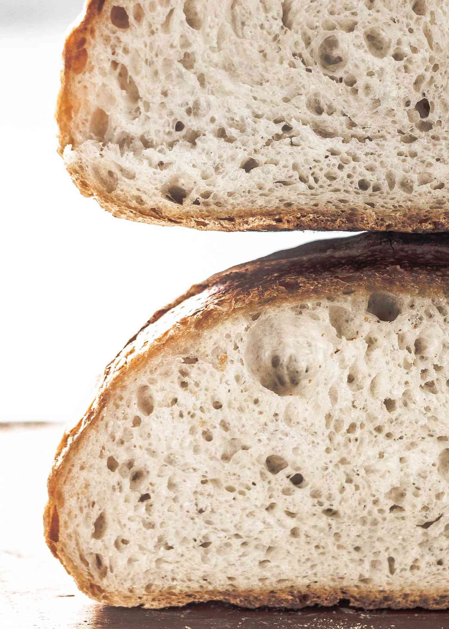 Close up of crusty homemade bread loaves stacked on top of each other. The bread has an airy crumb.