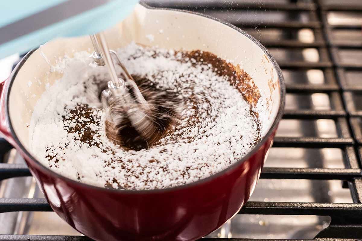 A hand mixer mixing frosting ingredients to make sheet cake.