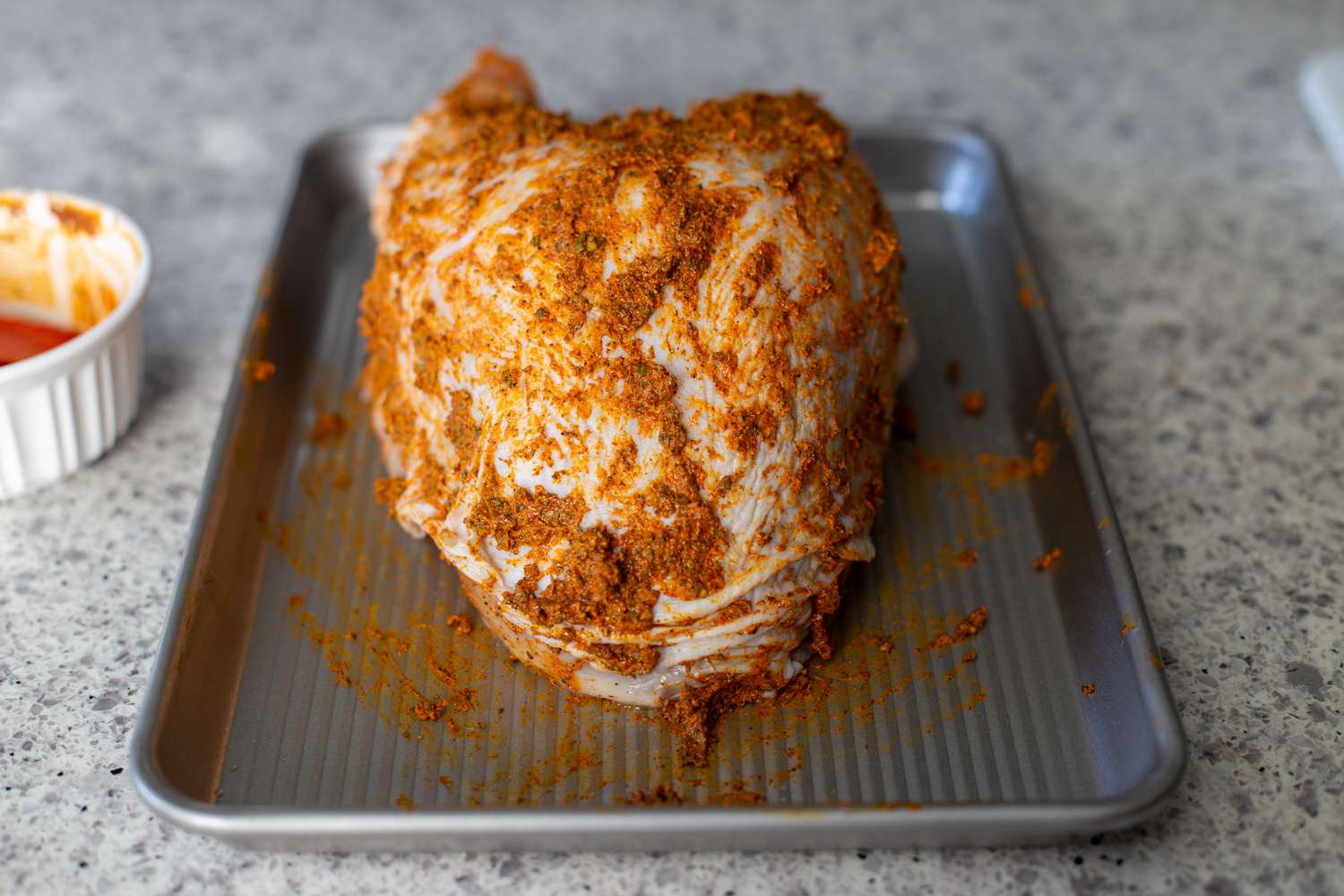 Turkey breast coated in seasoning and set on a baking sheet.